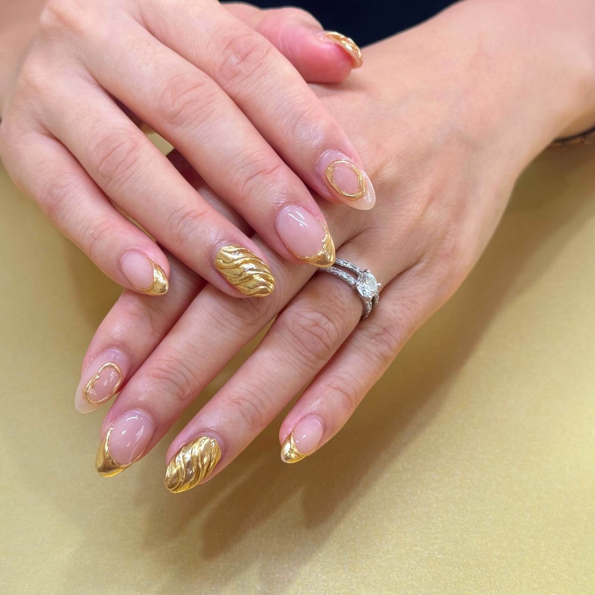 Sculpted metallic gold nail art on a glossy nude base